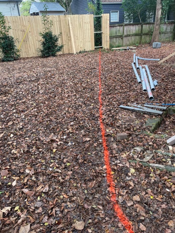 Backyard marked with orange line, near fence and construction materials.