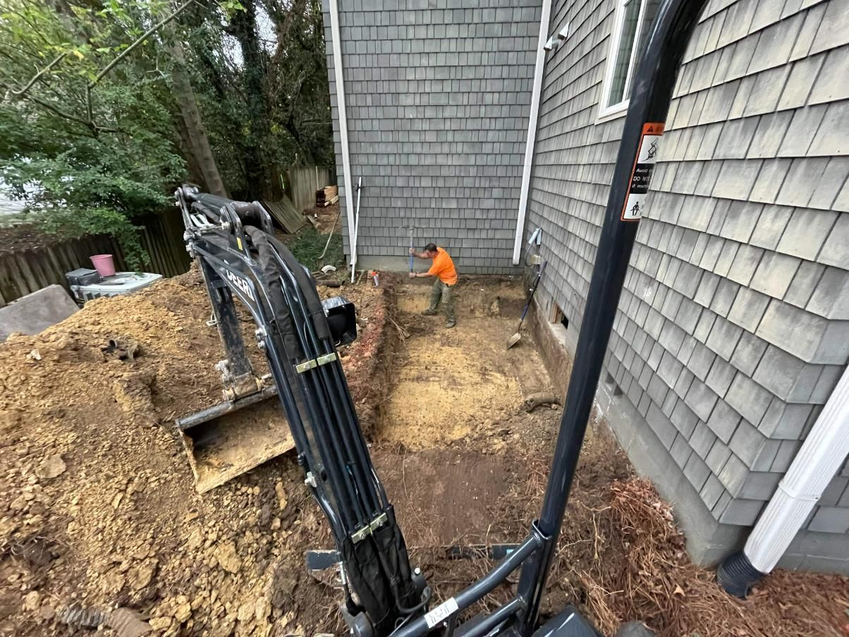 Construction site with excavator, worker in orange shirt, house with gray shingles.
