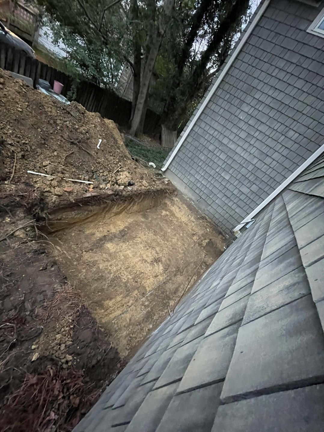 Eroded hillside next to a building with gray shingles and a tree in the background.