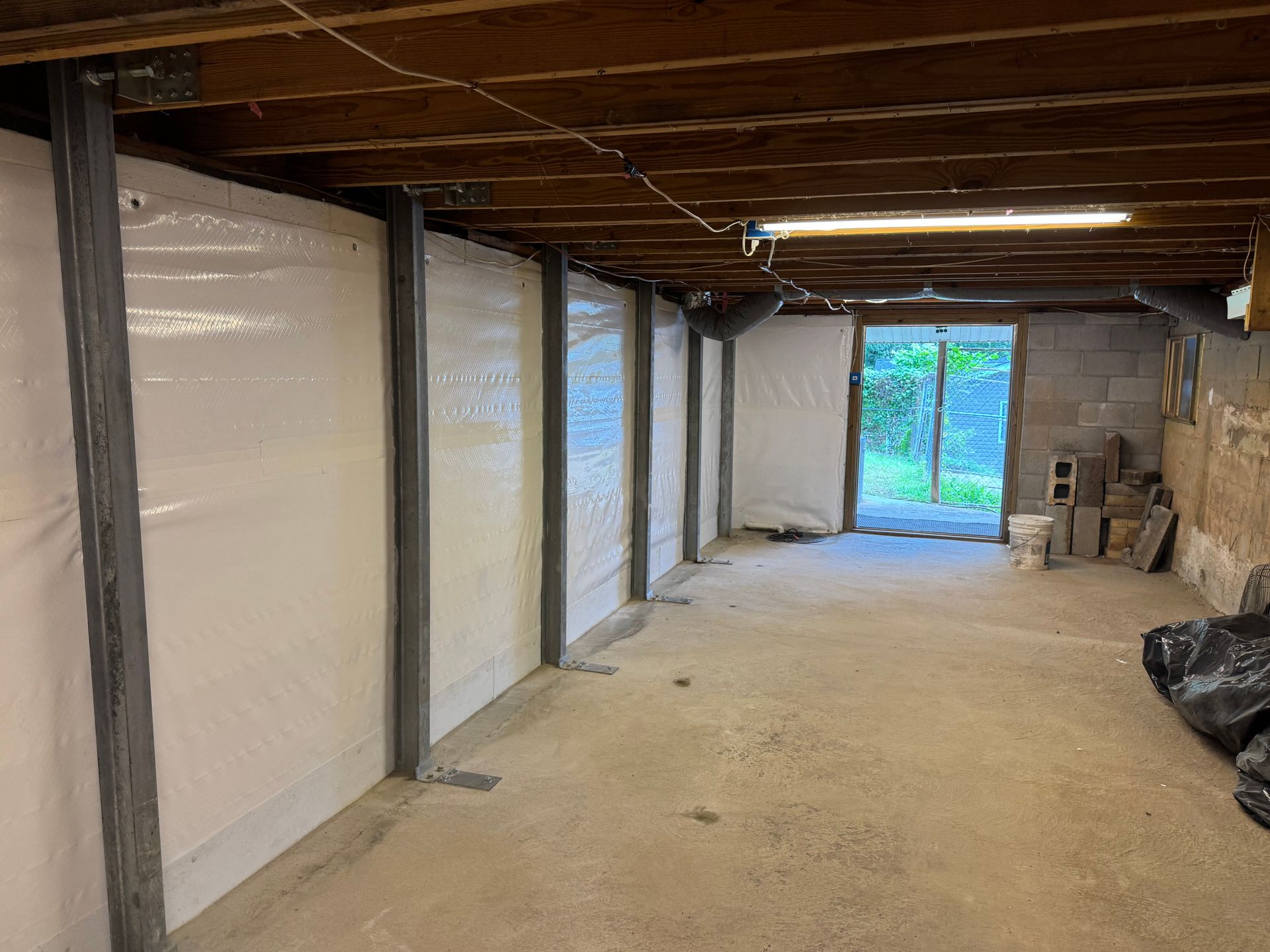 Basement with white wrapped walls and metal supports, leading to an open door and a yard.