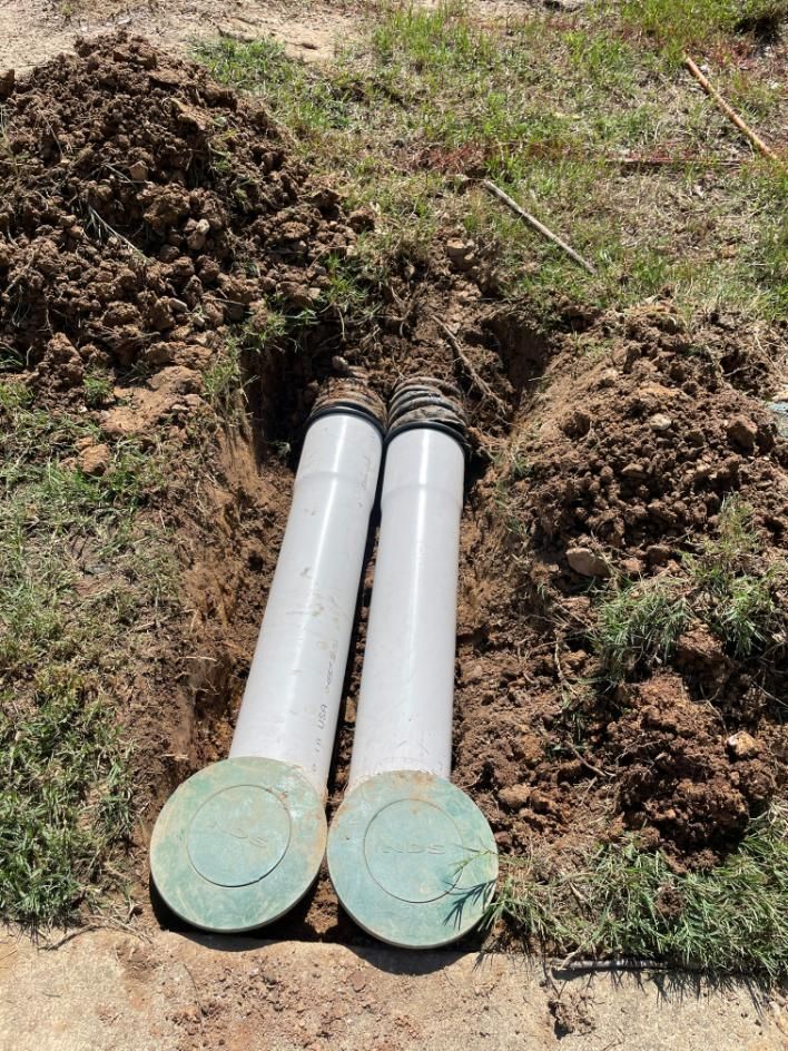 Two white pipes with green caps in a dirt trench, possibly for drainage.