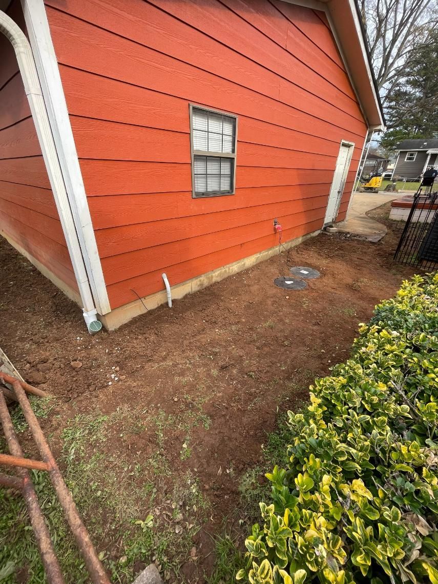 Red building with window and door, beside a brown mulch-covered yard with green hedge.