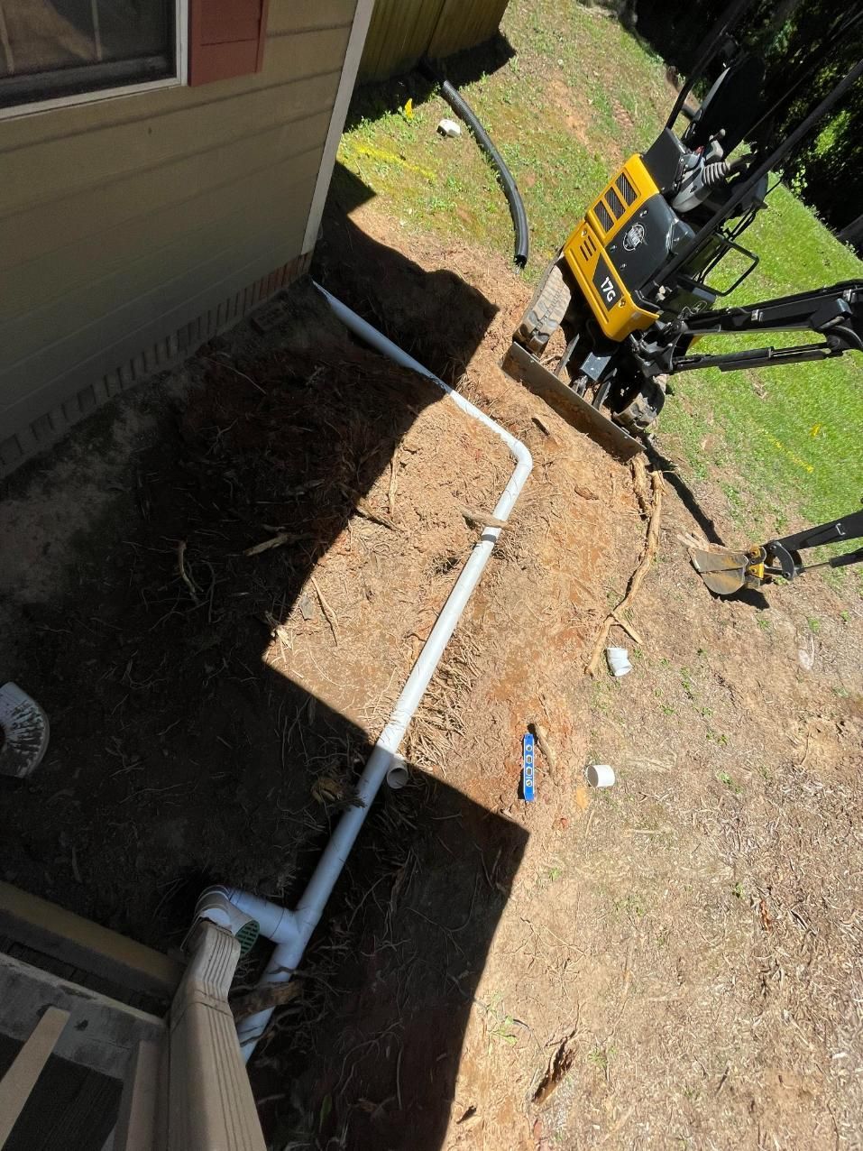 White PVC pipes being installed near a house foundation; a yellow machine is in the background.