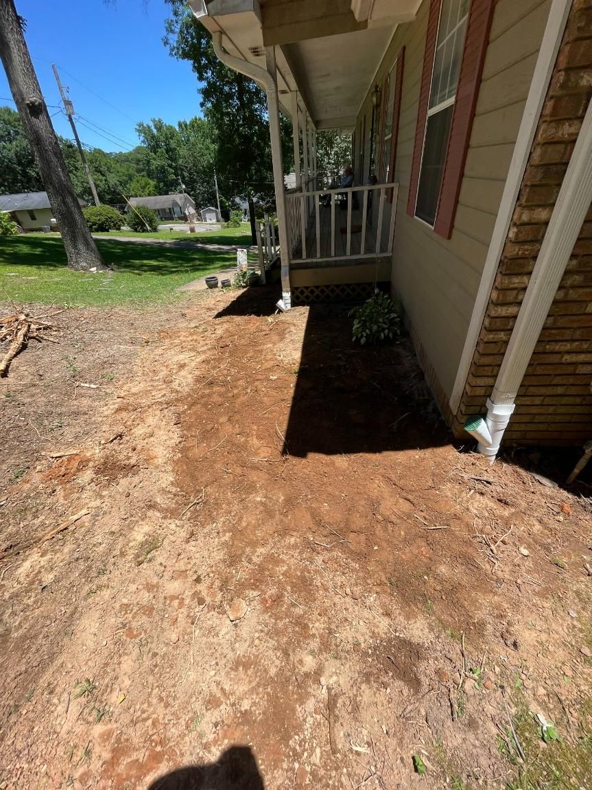 A dirt patch in front of a house. The house has beige siding, white gutters, and a porch.