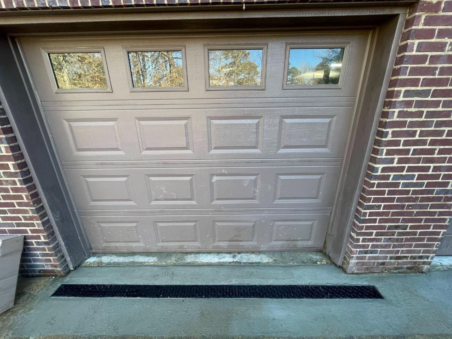 Brown garage door with windows, set in a brick building with a gray concrete apron.