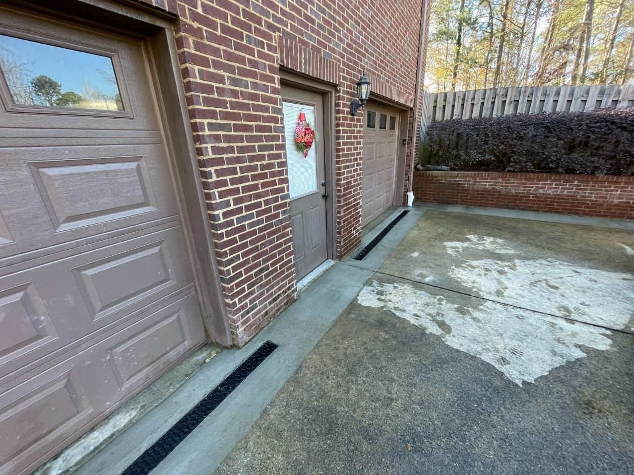 Brick building with garage doors and entrance. Black drainage channel on concrete.