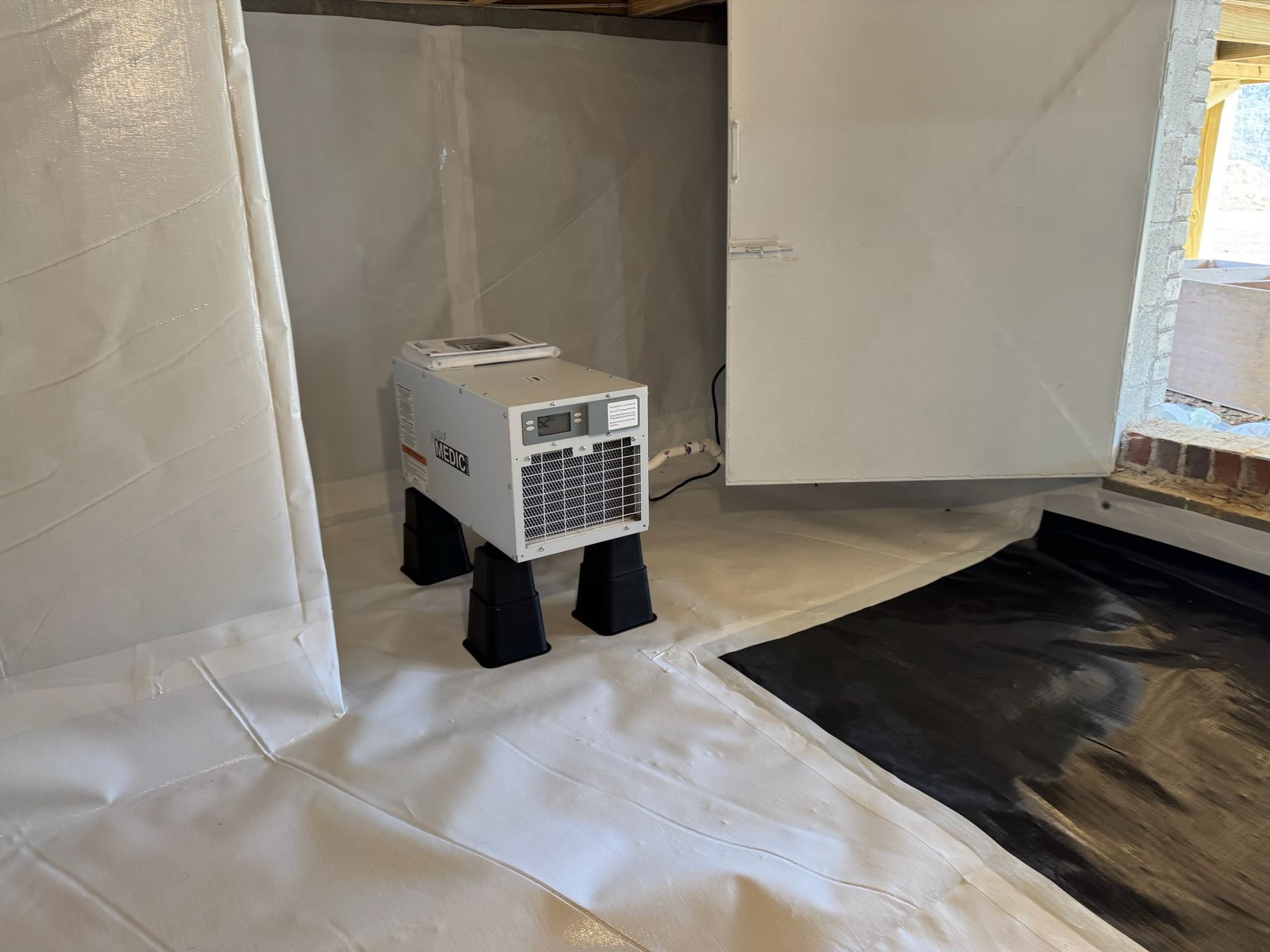 Crawl space with vapor barrier, supports, and metal beams under a house.