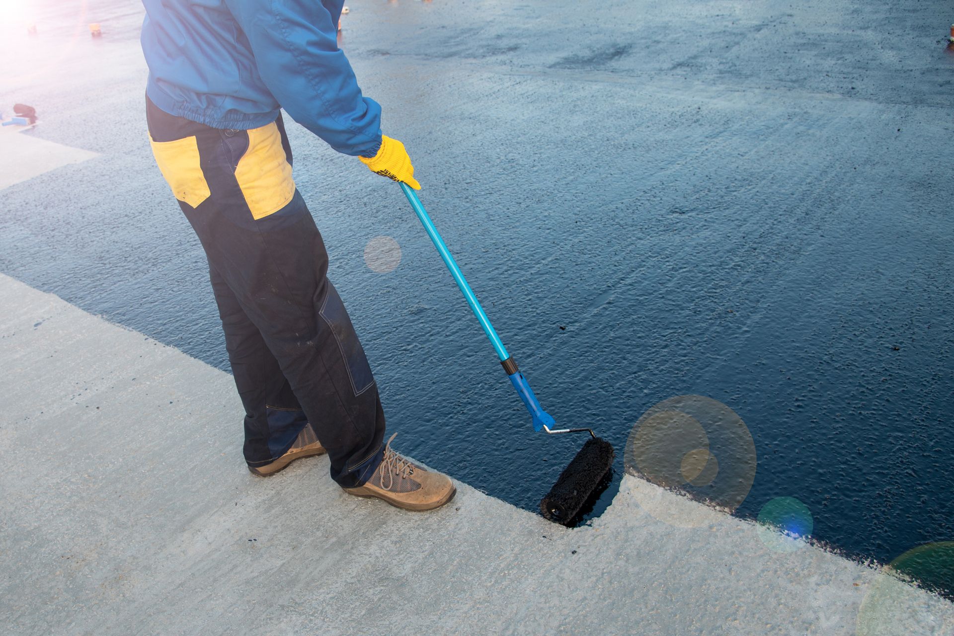 A Man is Painting a Road With a Roller