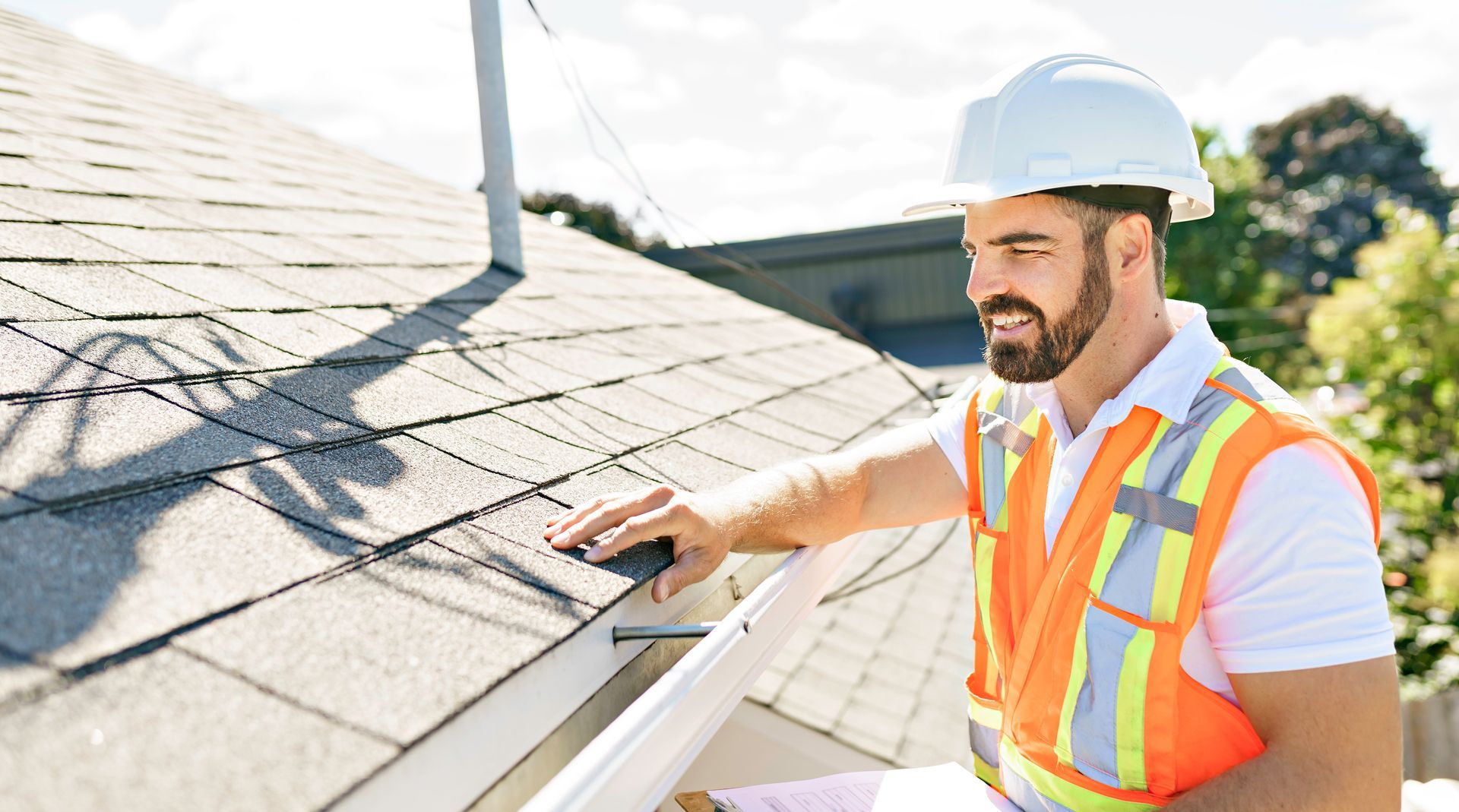 A Man Wearing a Hard Hat and Safety Vest is Working on a Roof