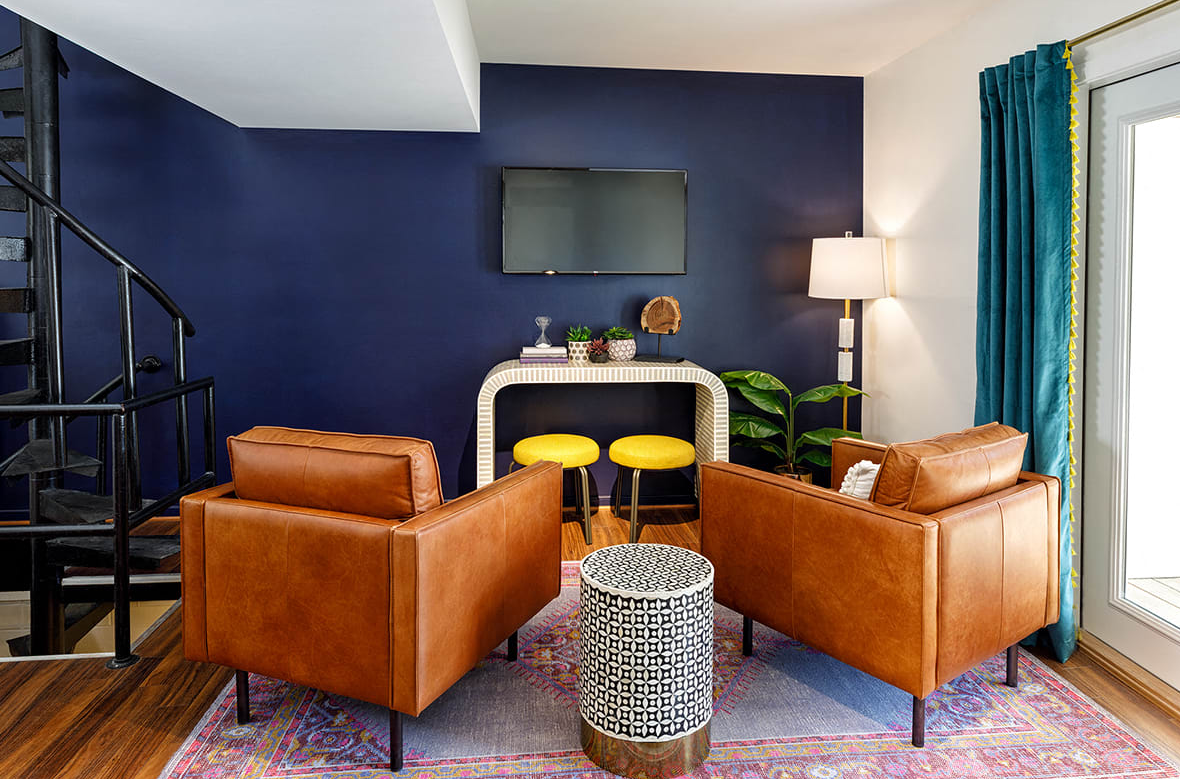 A living room with two chairs , a table , a television and a spiral staircase.