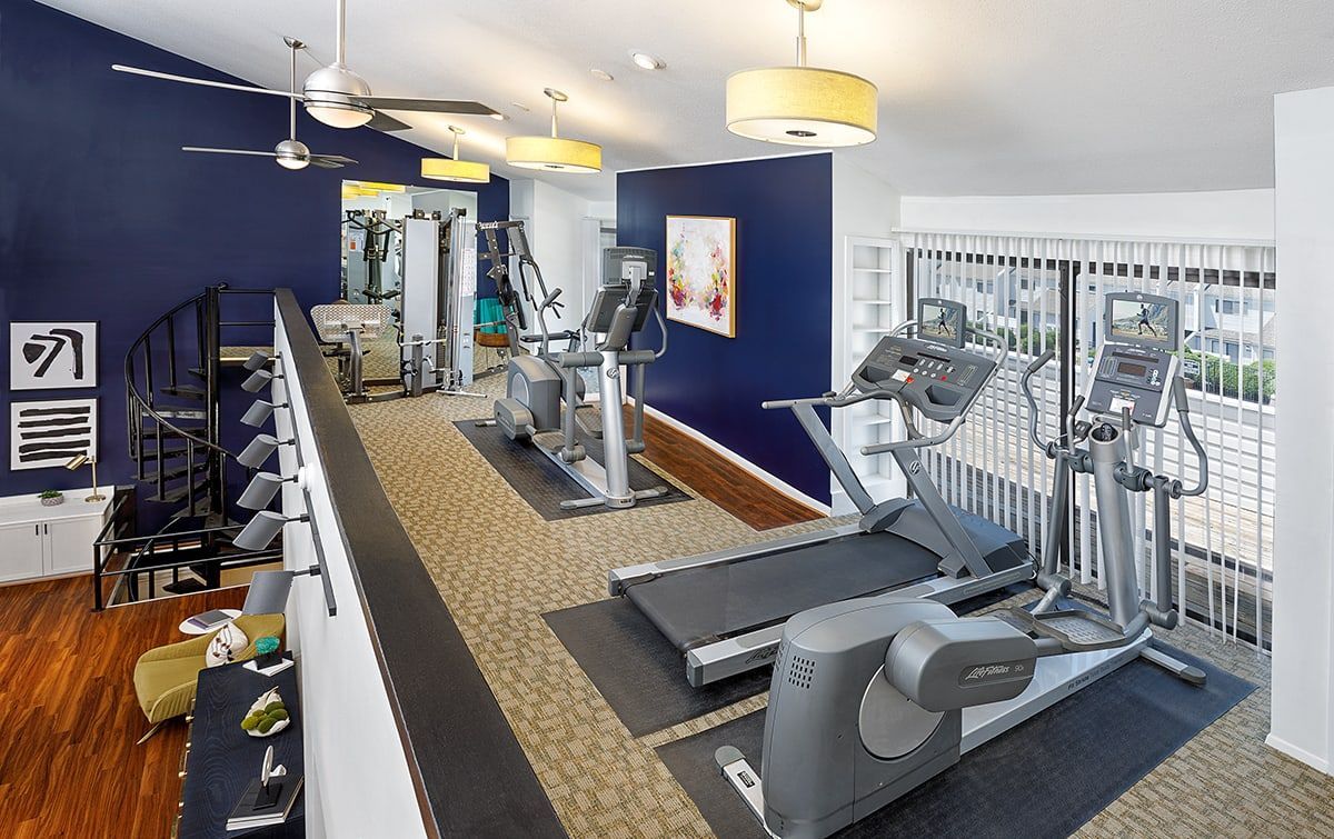 A gym with treadmills , exercise bikes , and a ceiling fan.