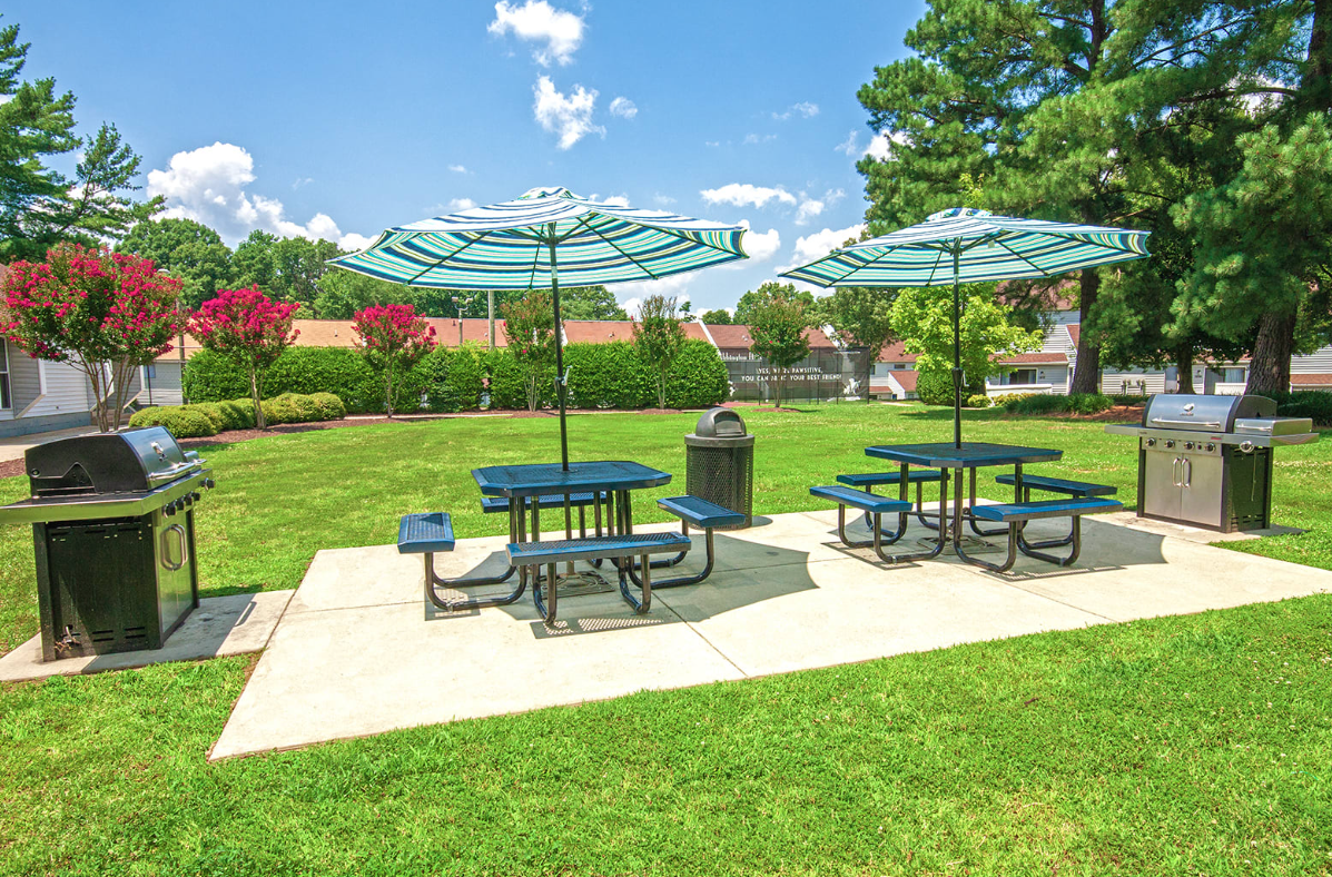 A picnic area with tables and umbrellas in a park.