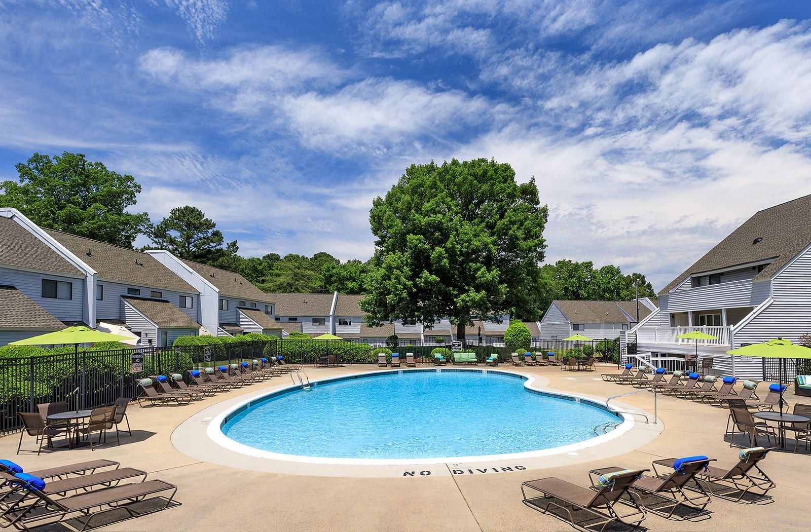A large swimming pool surrounded by chairs and umbrellas in a residential area.