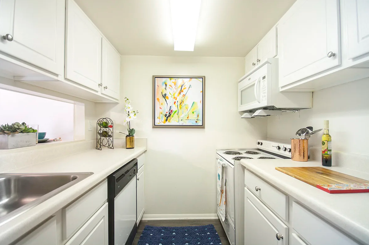 A kitchen with white cabinets , stainless steel appliances , a sink , and a painting on the wall.