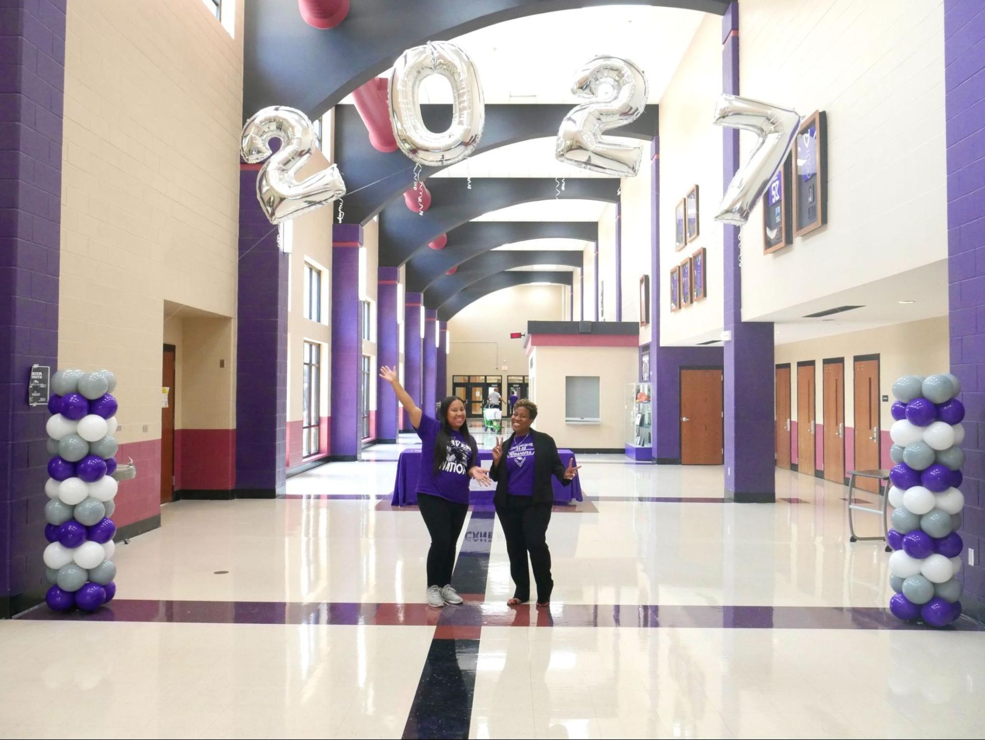 Two women are standing in a hallway with balloons hanging from the ceiling.