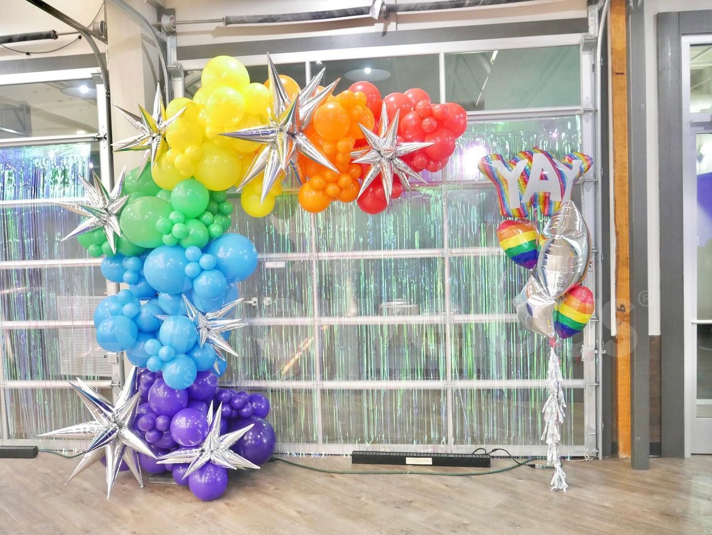 A rainbow colored balloon arch is sitting in front of a garage door.
