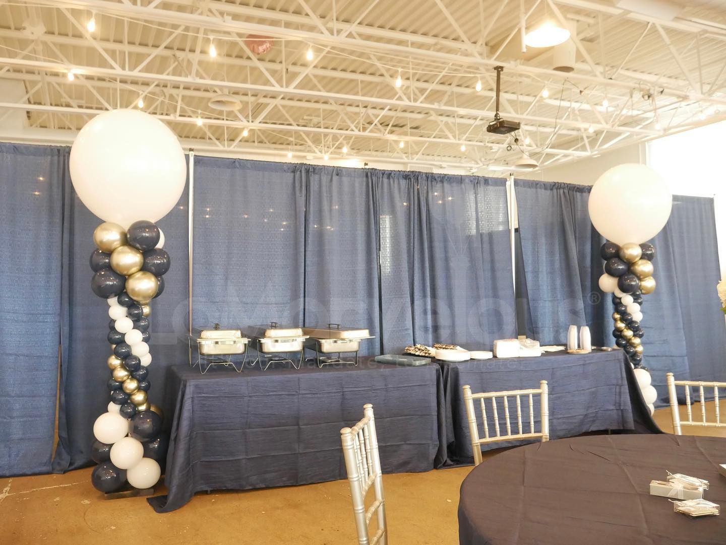A room with tables and chairs and balloons on the pillars