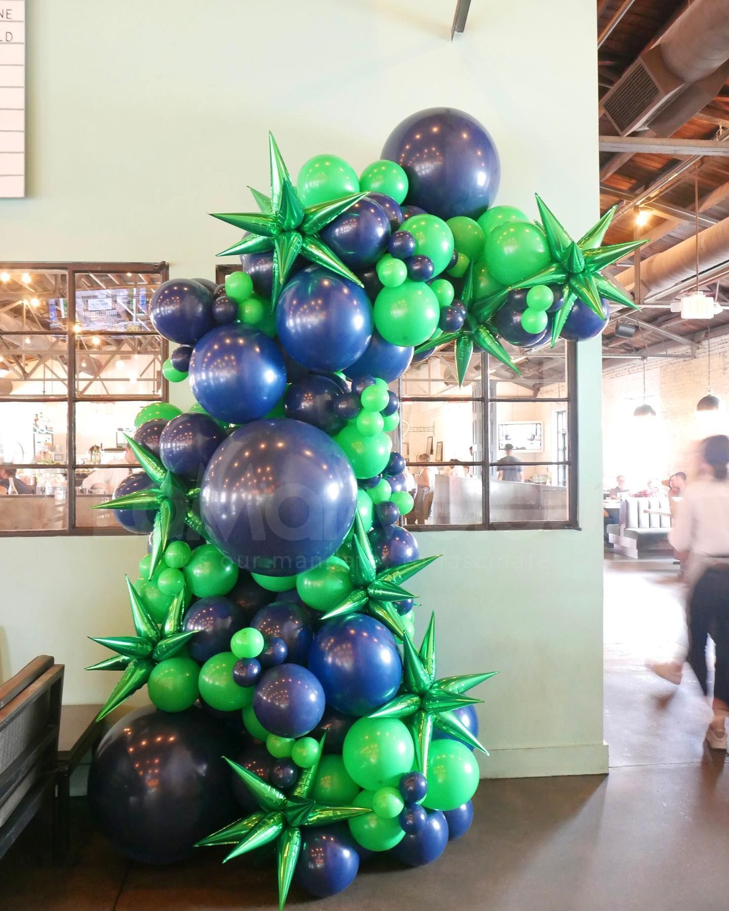A bunch of blue and green balloons are stacked on top of each other in a room.