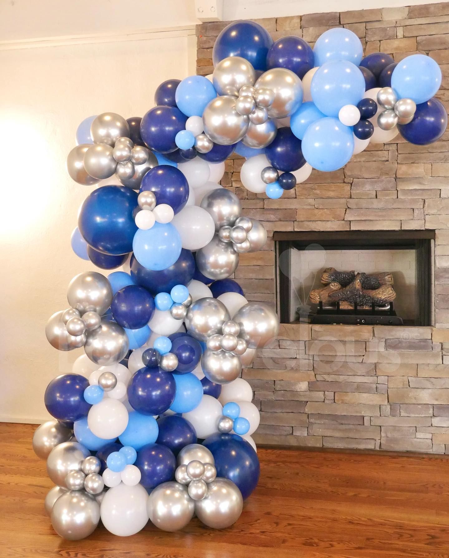A bunch of blue and silver balloons are sitting in front of a fireplace.