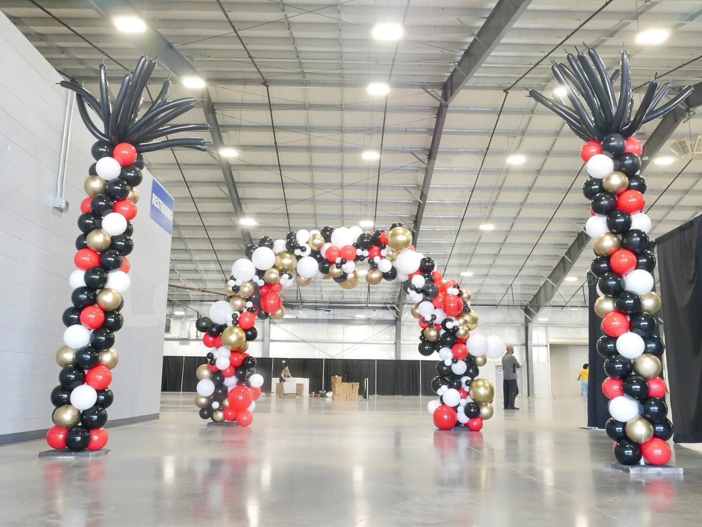 A red , white , and gold balloon arch in a warehouse.
