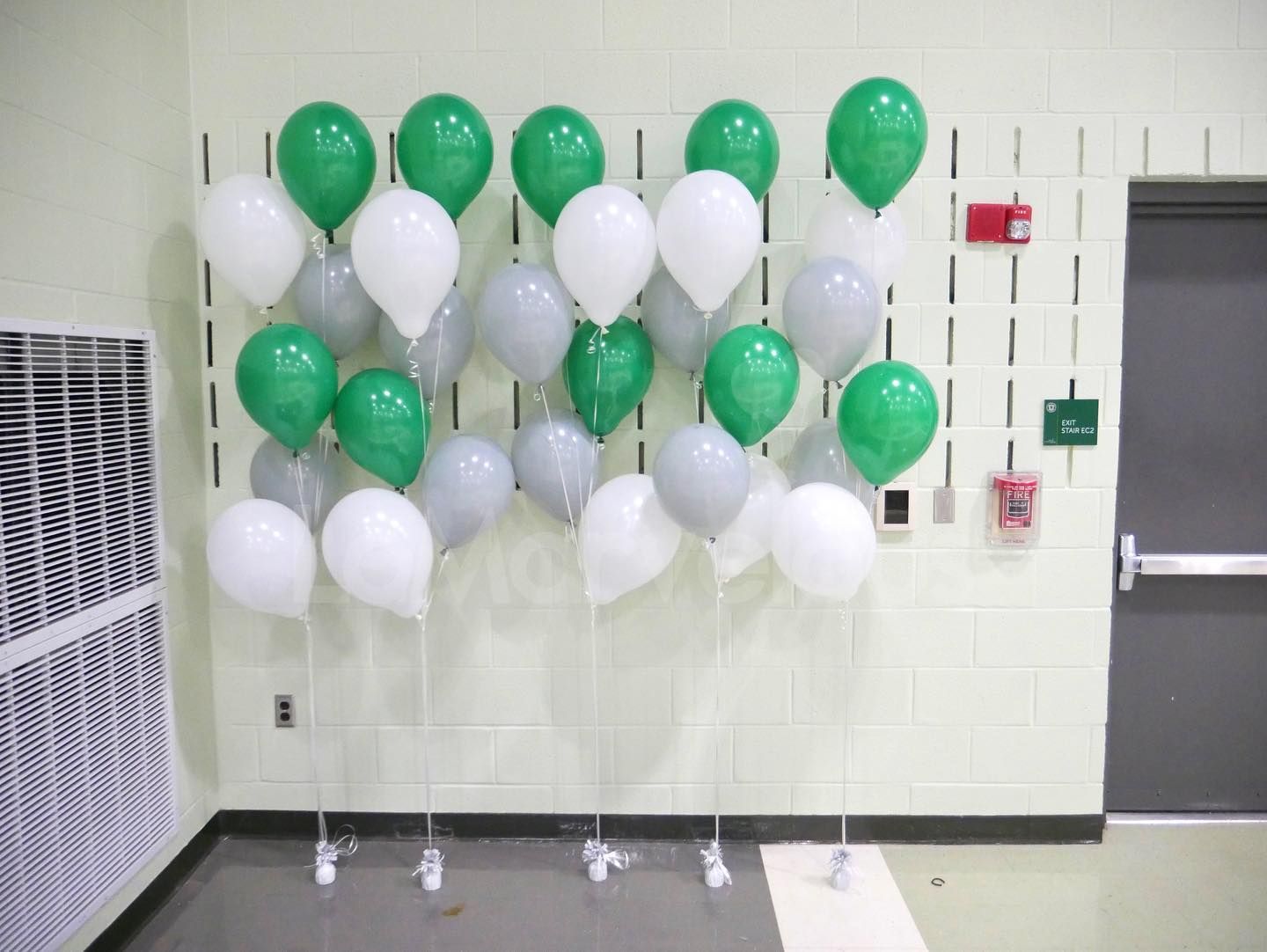 A bunch of green white and gray balloons hanging on a wall
