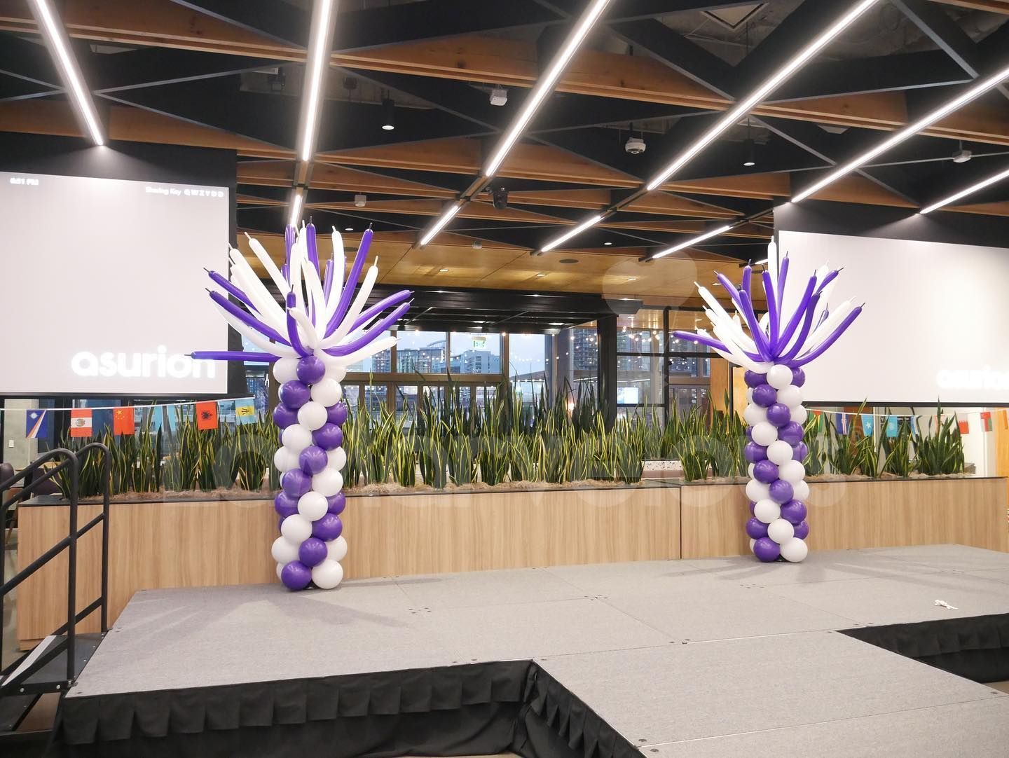 A stage with purple and white balloons in the shape of palm trees.