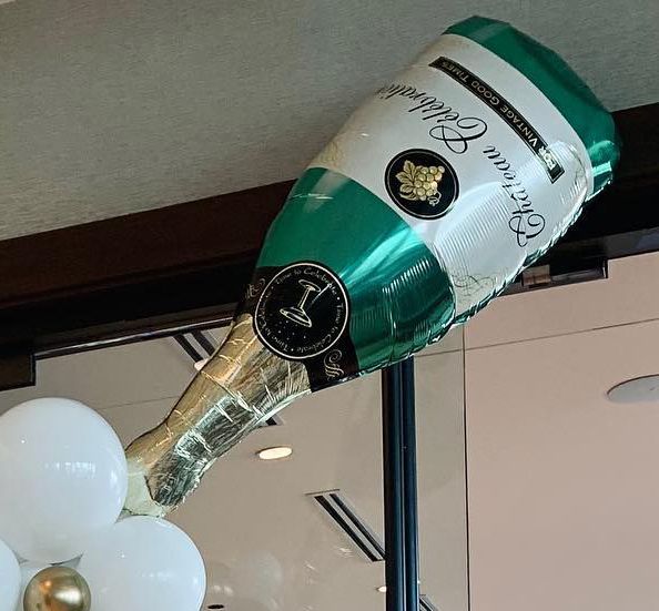 A green and white balloon in the shape of a bottle of champagne