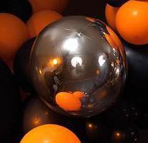 A bunch of orange and black balloons with a clear ball in the middle.