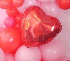 A red heart shaped balloon is surrounded by pink and red balloons.