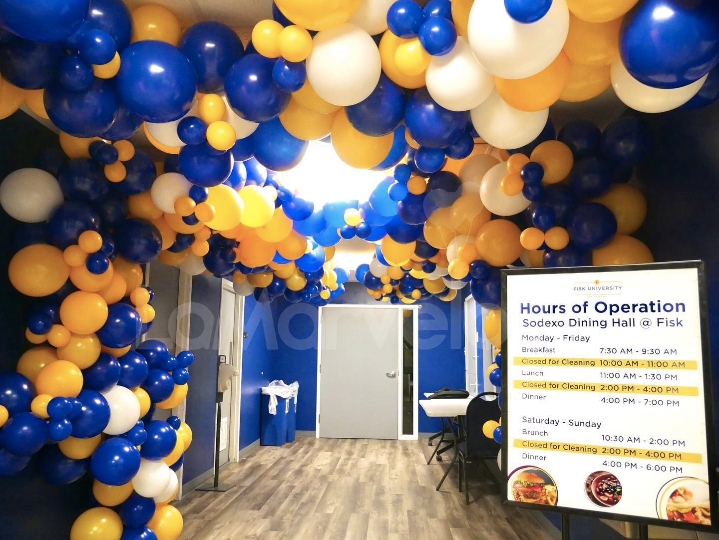 A hallway filled with blue and yellow balloons and a sign that says hour of operation