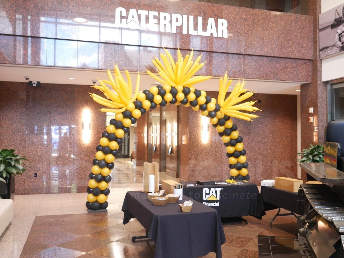 A yellow and black balloon arch in front of a caterpillar building