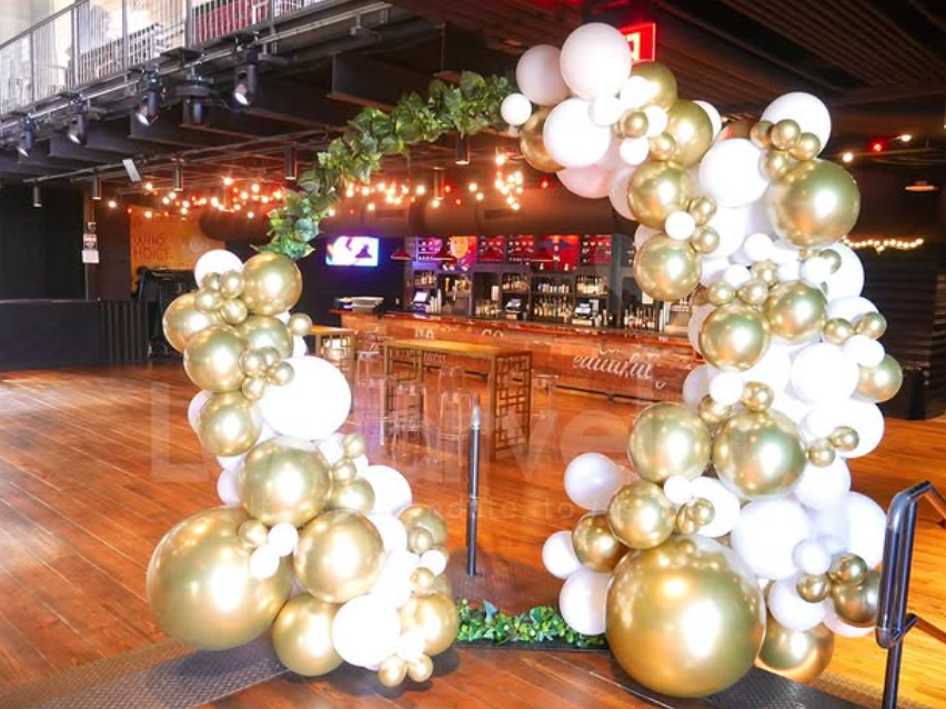 A large arch made of gold and white balloons in an empty room.