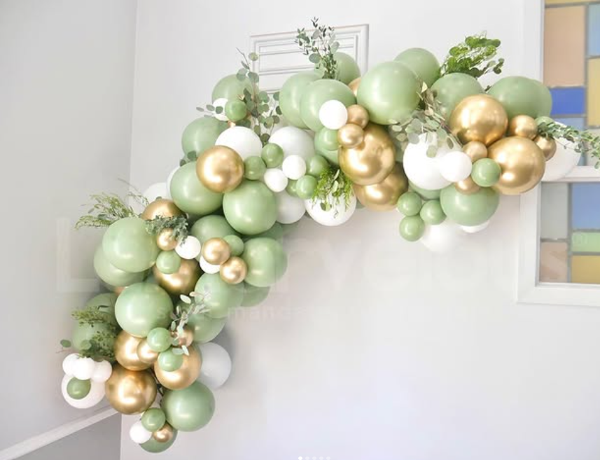 A bunch of green and gold balloons are hanging on a wall.