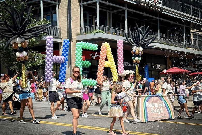 A group of people are walking down a street with balloons in the shape of the word heal.