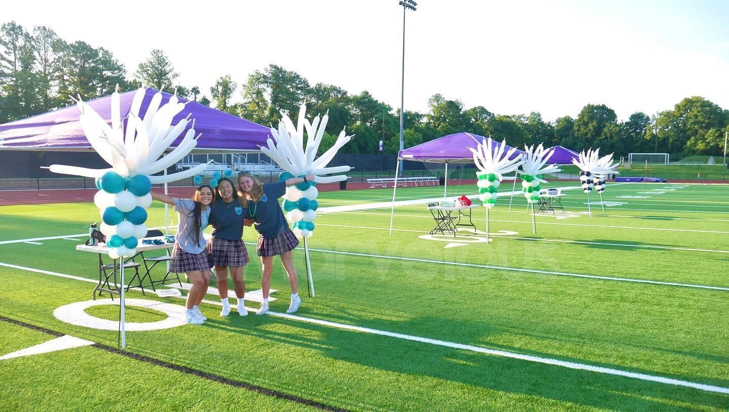 Three girls are standing on a football field with balloons.
