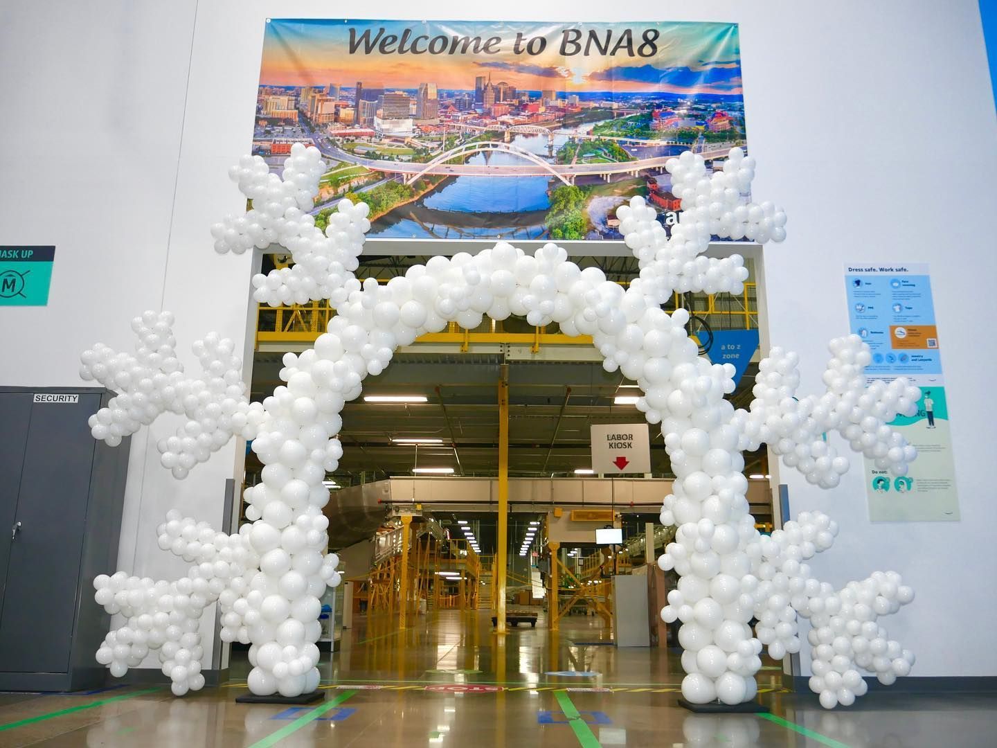 A large arch made of white balloons and snowflakes in a warehouse.