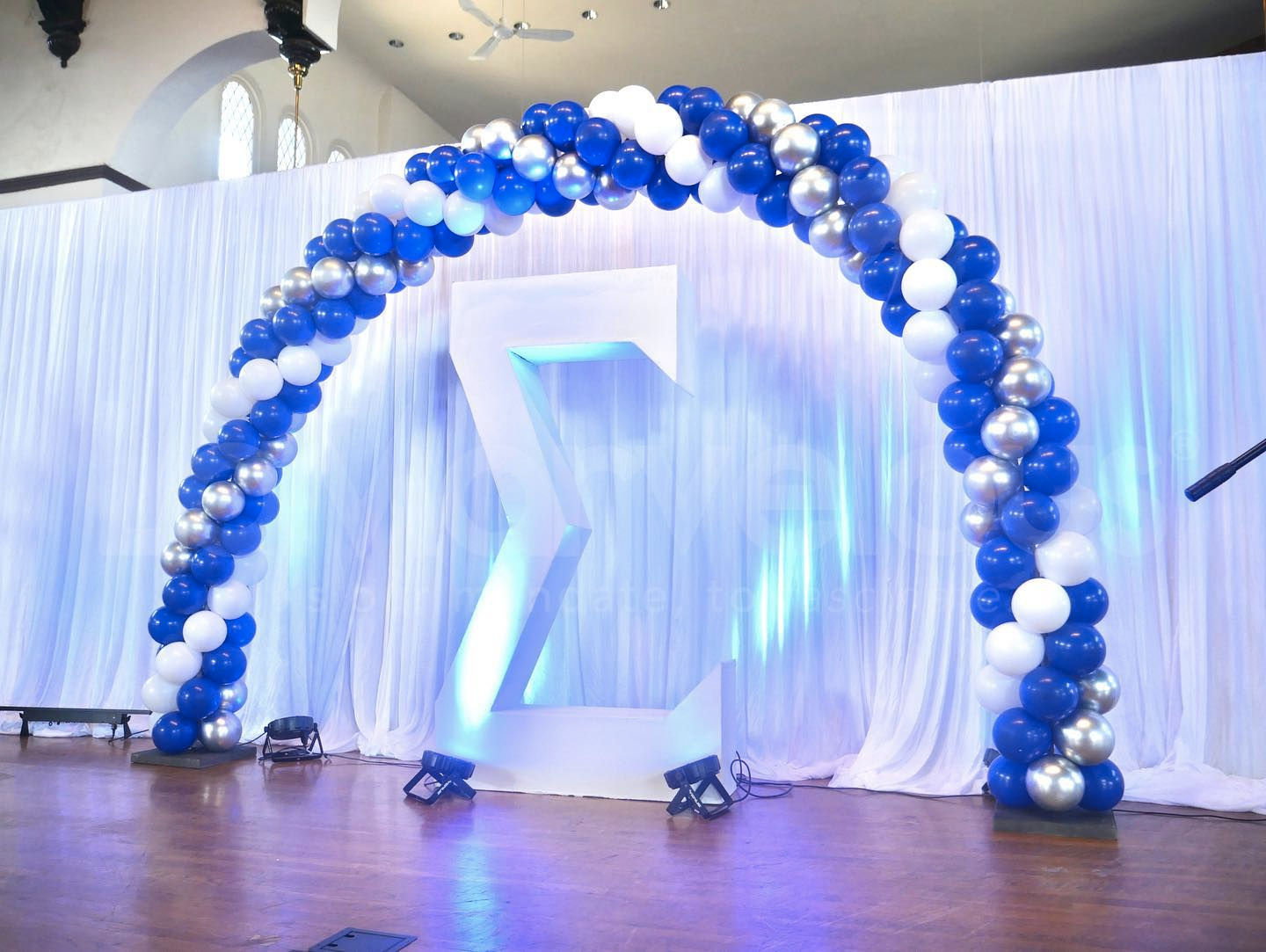 A blue and white balloon arch with a sigma symbol in the background