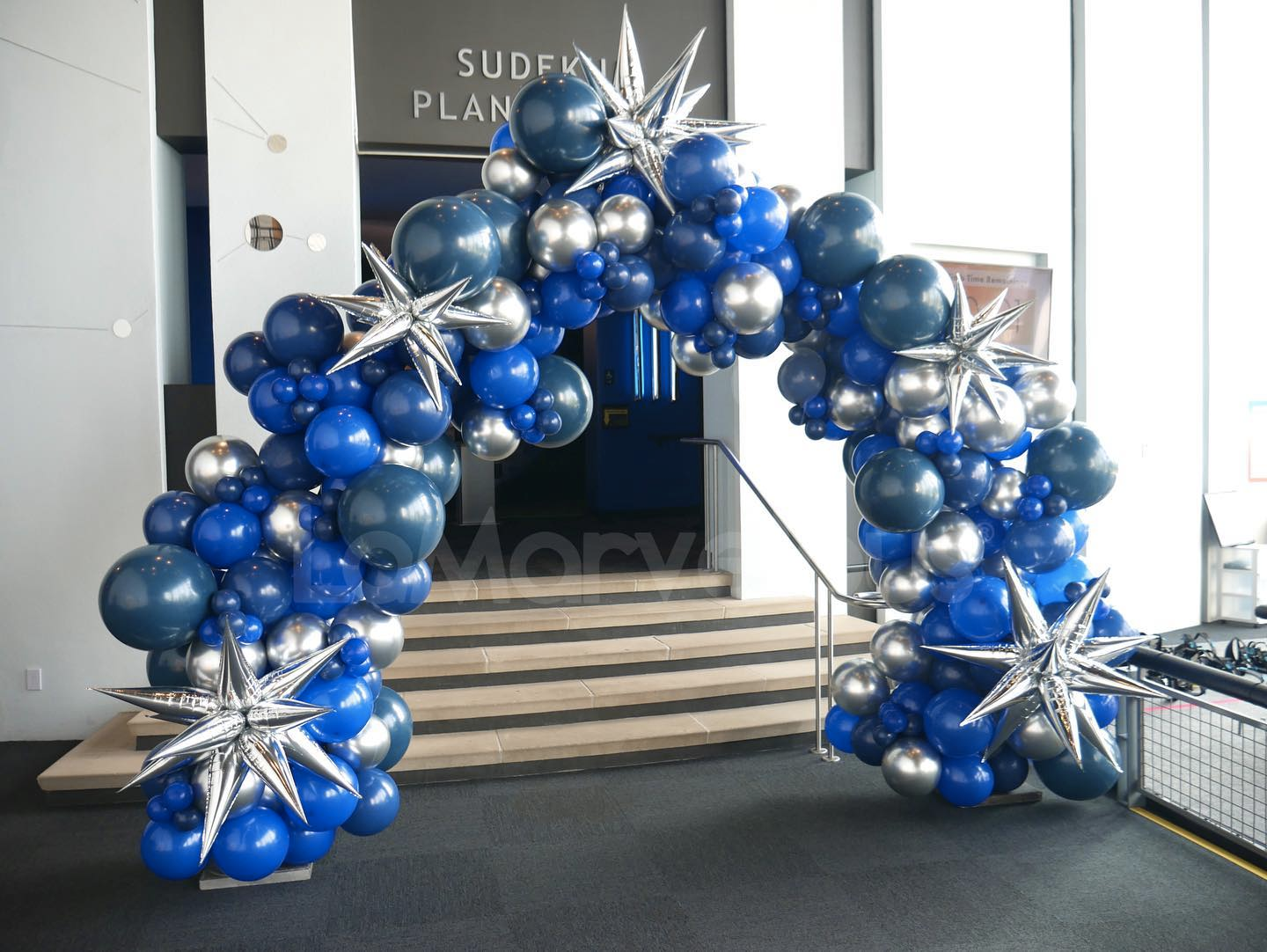 A blue and silver balloon arch in front of a building