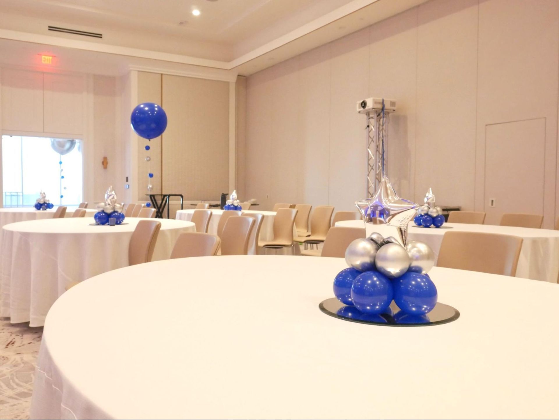 A room with tables and chairs decorated with blue and silver balloons.