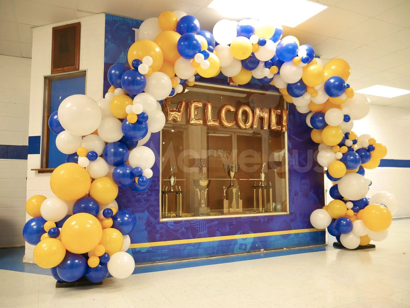A welcome sign is surrounded by blue and yellow balloons