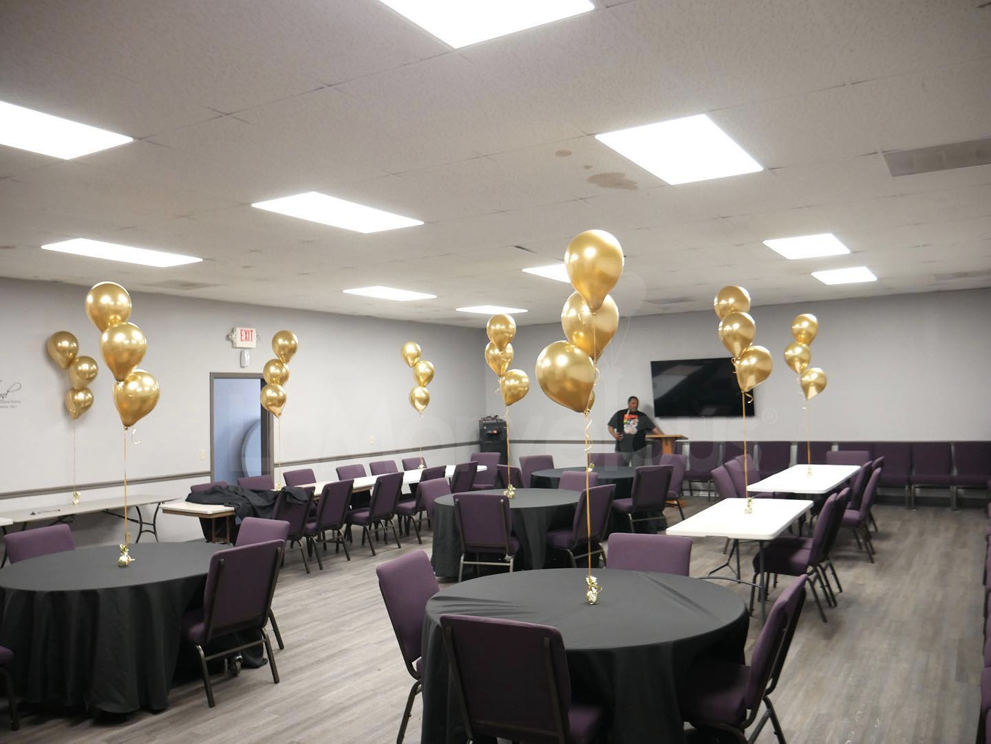 A large room with tables and chairs and balloons hanging from the ceiling