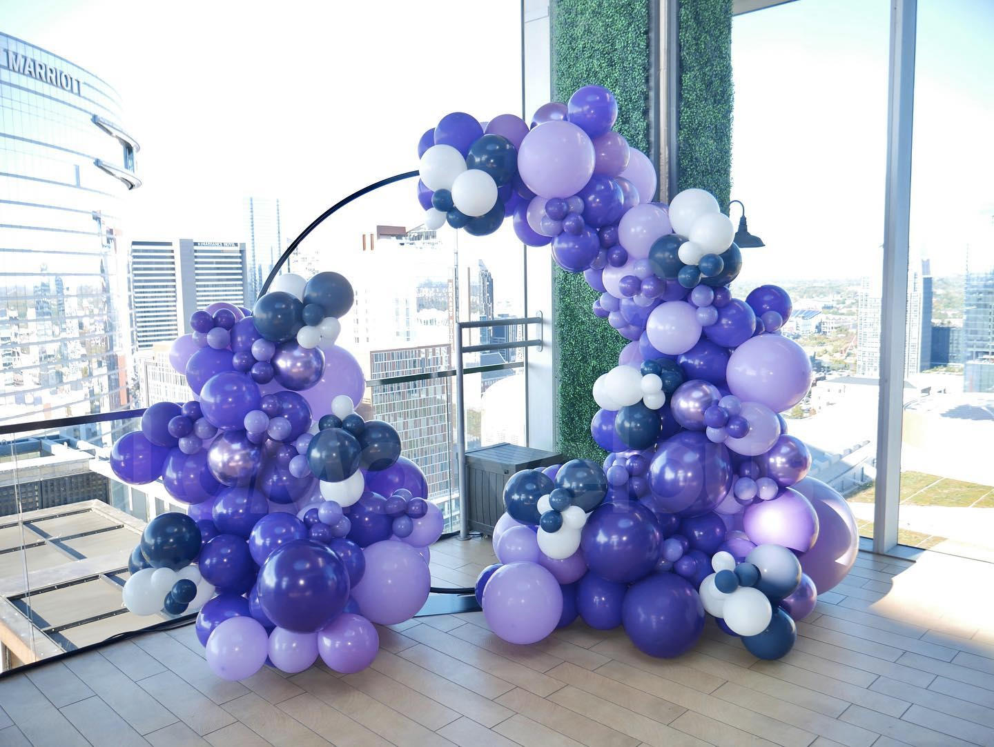 A bunch of purple balloons are sitting on a wooden floor in front of a window.