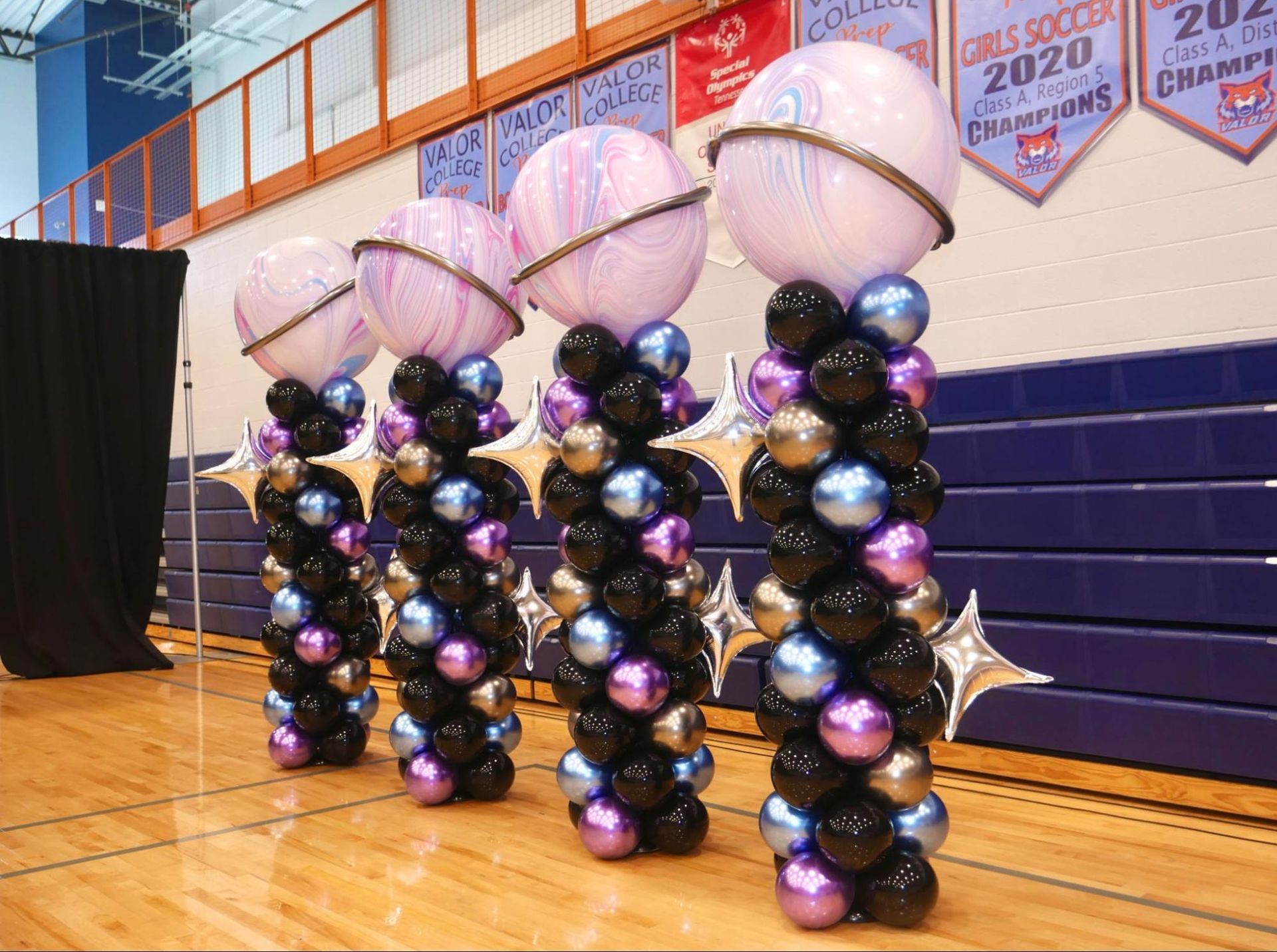 A row of balloons are lined up on a wooden floor in a gym.