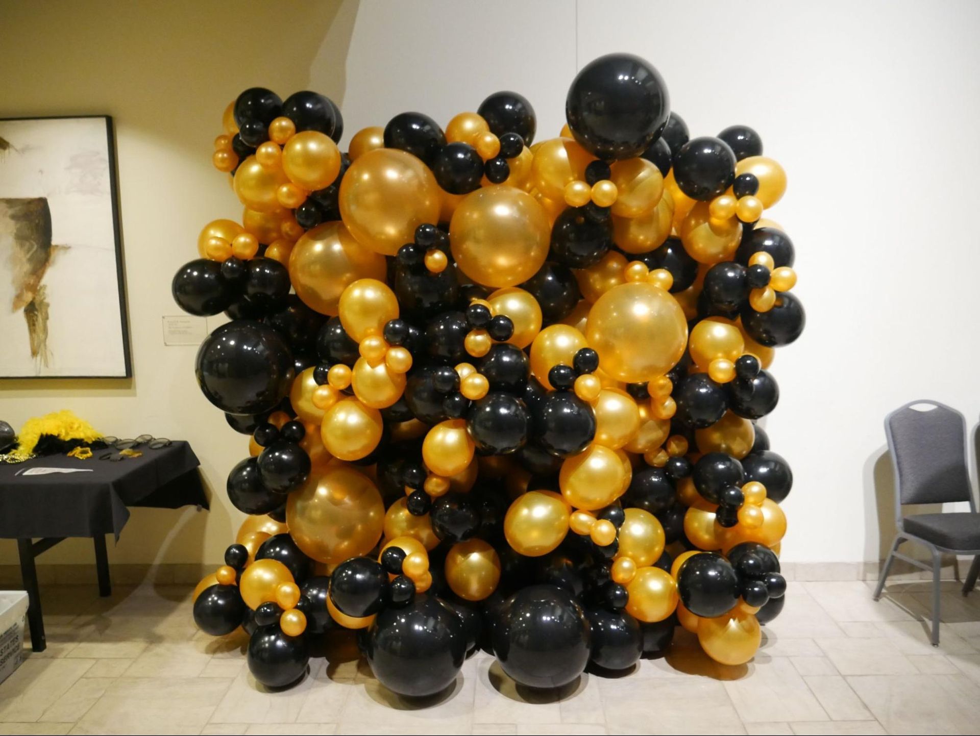 A wall filled with black and gold balloons in a room.