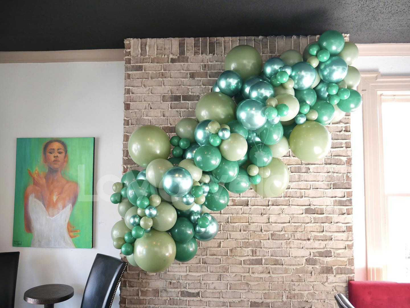 A bunch of green balloons are hanging from a brick wall.