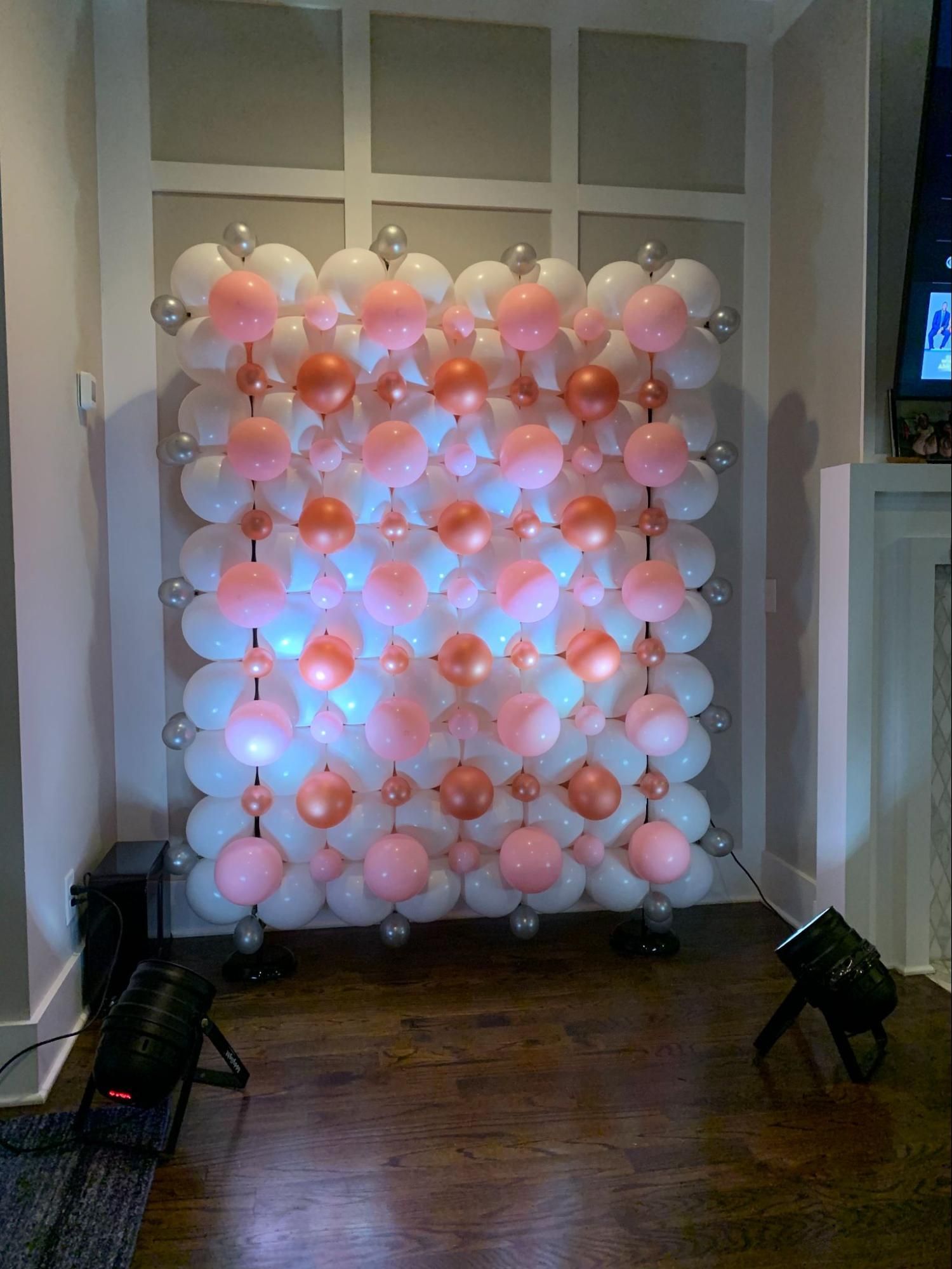 A wall of pink and white balloons in a living room.