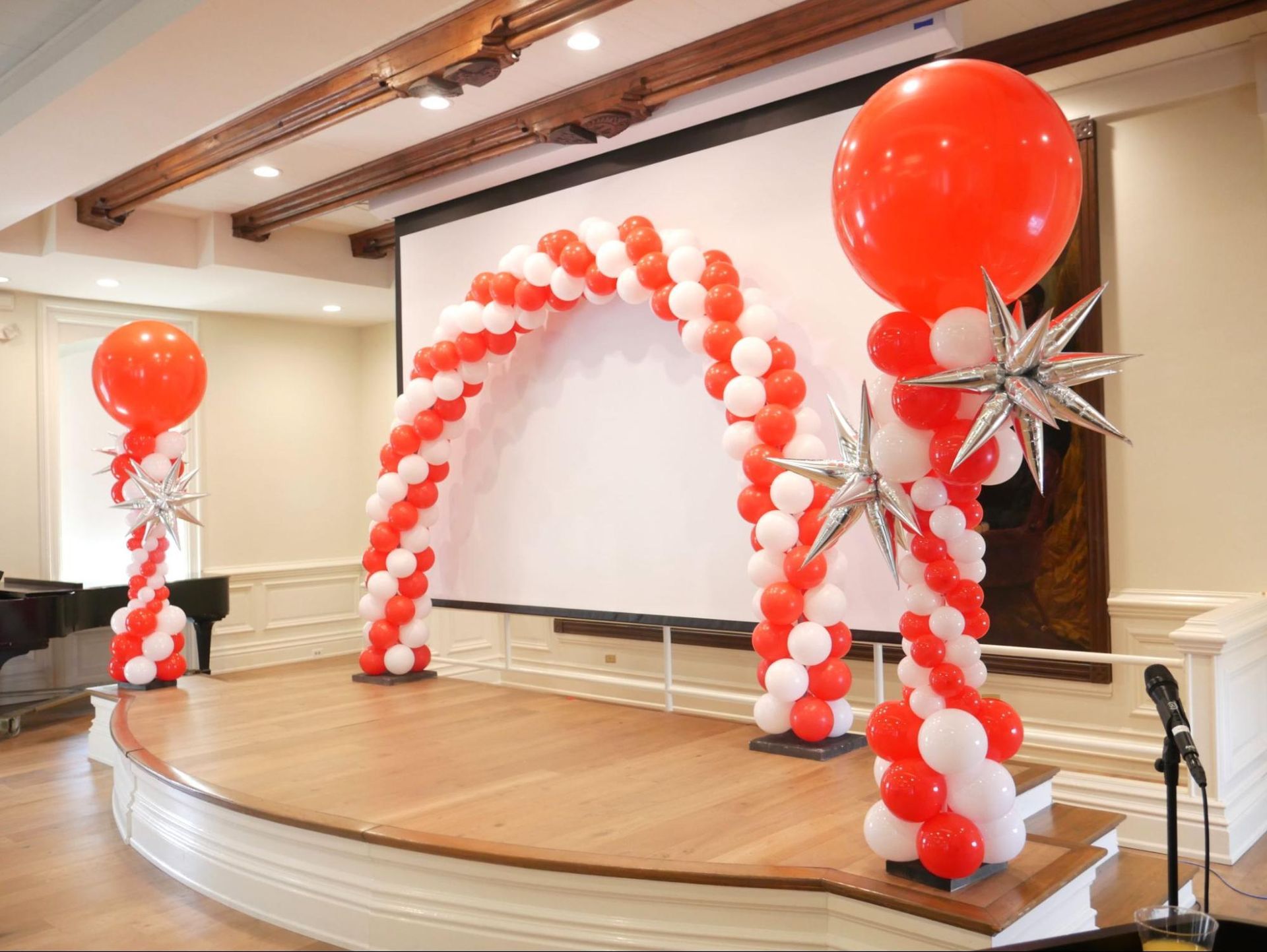 A stage decorated with red and white balloons and a projector screen.