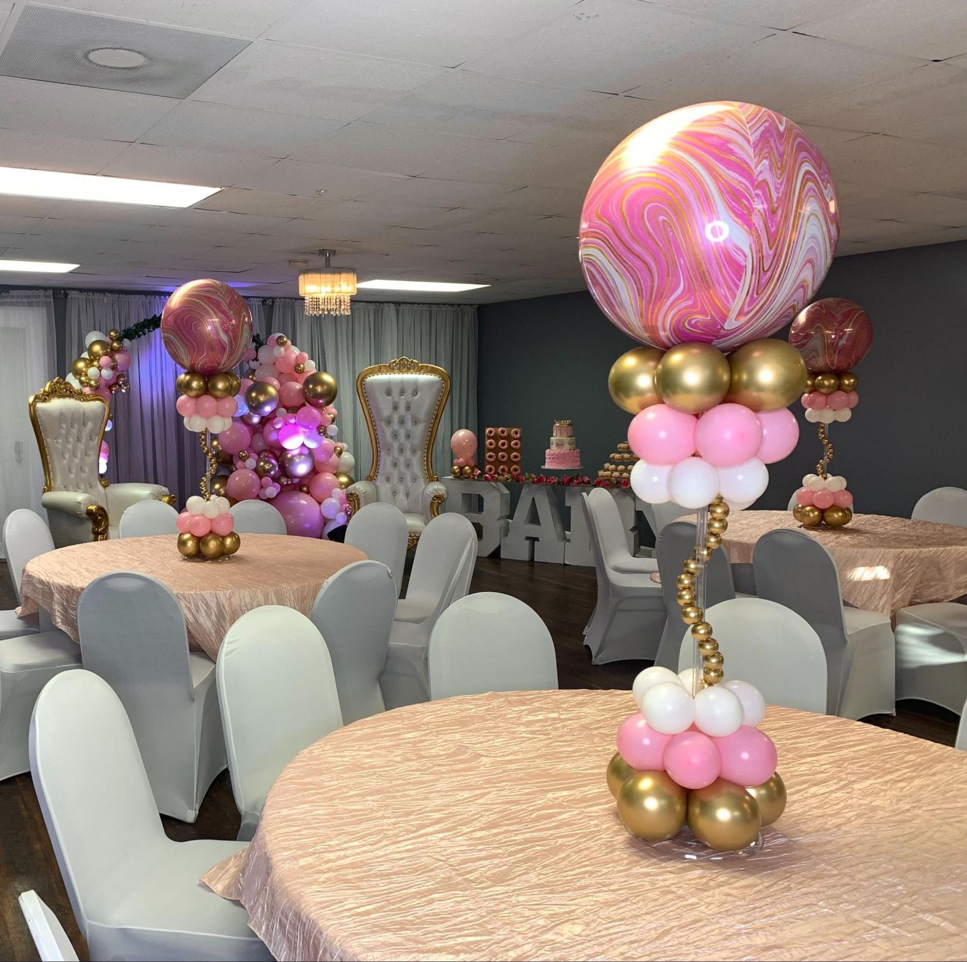 A room with tables and chairs decorated with pink and gold balloons