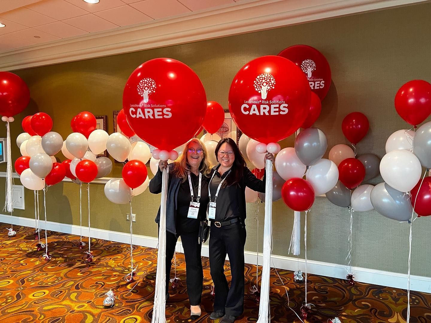 Two women are standing next to large red balloons that say cares