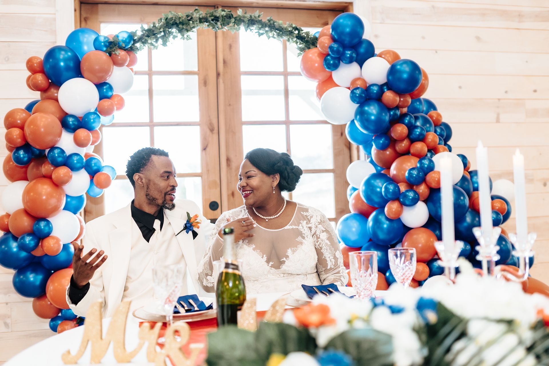 A bride and groom are sitting at a table with balloons in the background.